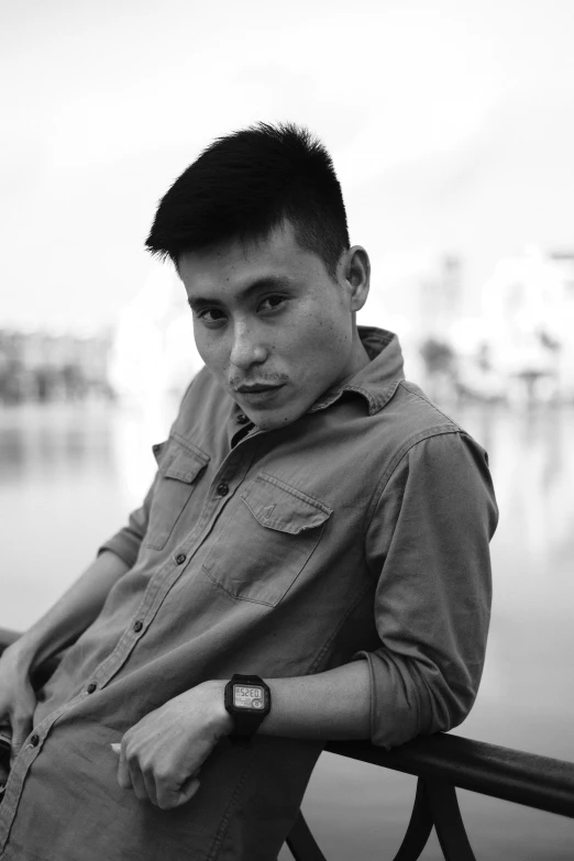 a boy is sitting on a bench in front of water