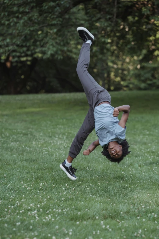 young black man doing hand stand in grass with trees in background