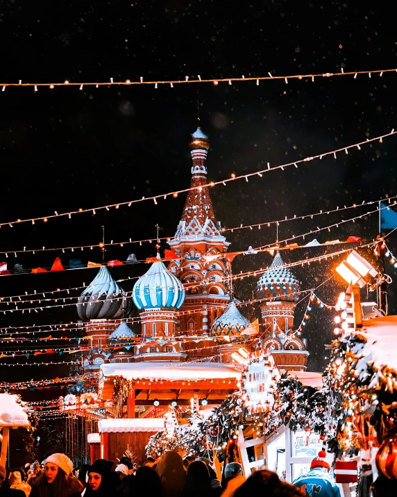 a crowd of people in a city with a building decorated with christmas lights