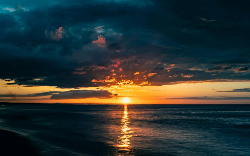 the sun rises as clouds gather in front of water