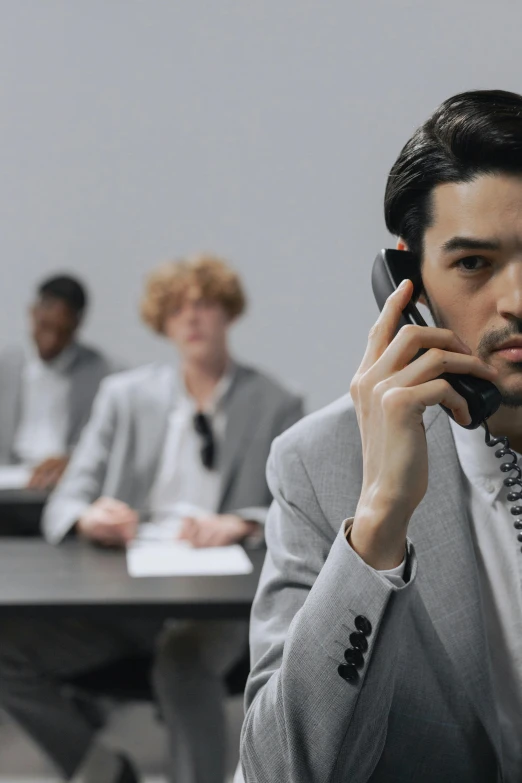 a man in business clothes using a cellphone to talk to another guy at the table