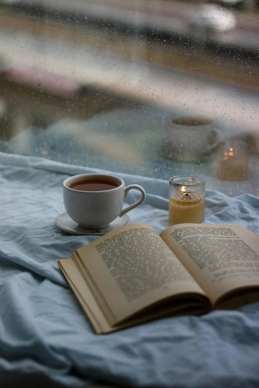 a book and cup on top of a bed with an open book