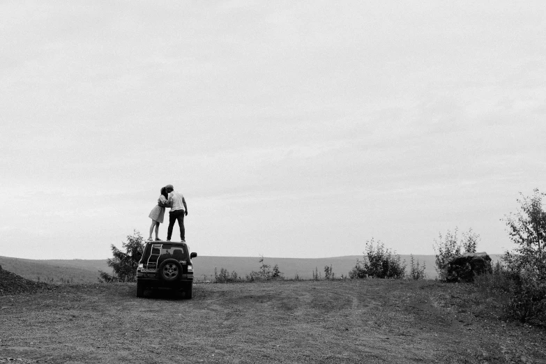 two people are on top of a car on a hill