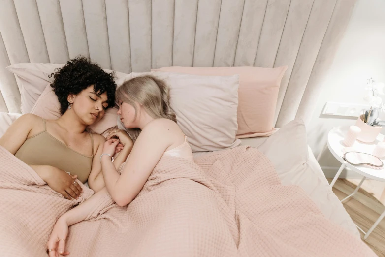 two women cuddle on the bed in their pink bedding