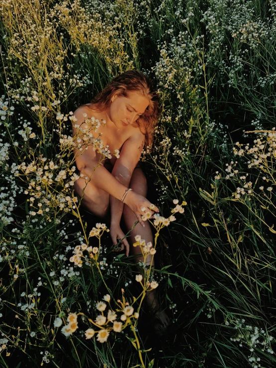 a girl sitting in tall grass and wild flowers