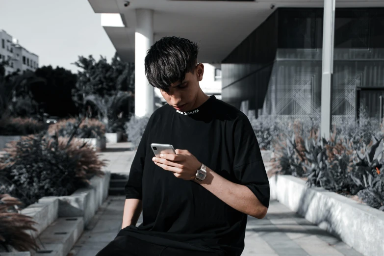 a young man sitting on a sidewalk and looking at his cellphone