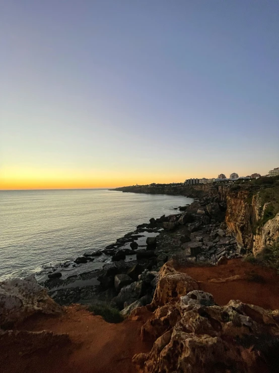 the shore is next to a cliff and has trees on top