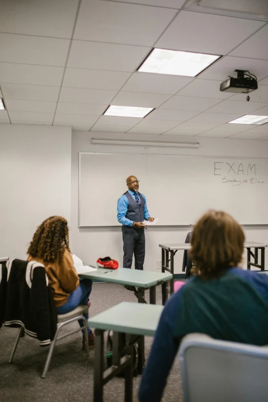 a man stands in front of a classroom as two students watch