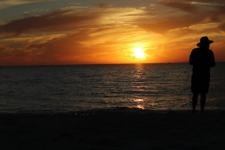 the silhouette of a man stands on the beach as the sun sets