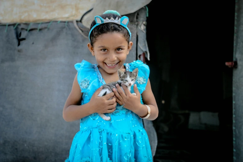 a little girl is holding a kitten wearing blue
