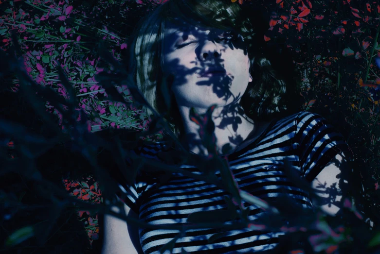 a woman with green hair and a  shirt posing for the camera in the shade of a leaf - laden tree