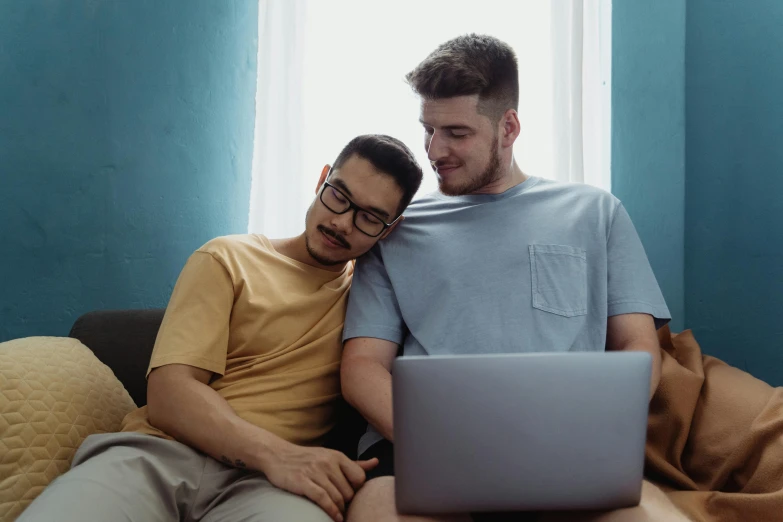 two men in yellow shirts are on a couch looking at their laptop