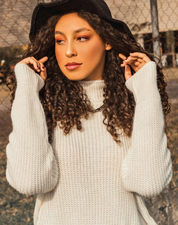 a woman is holding her hair while wearing a white sweater