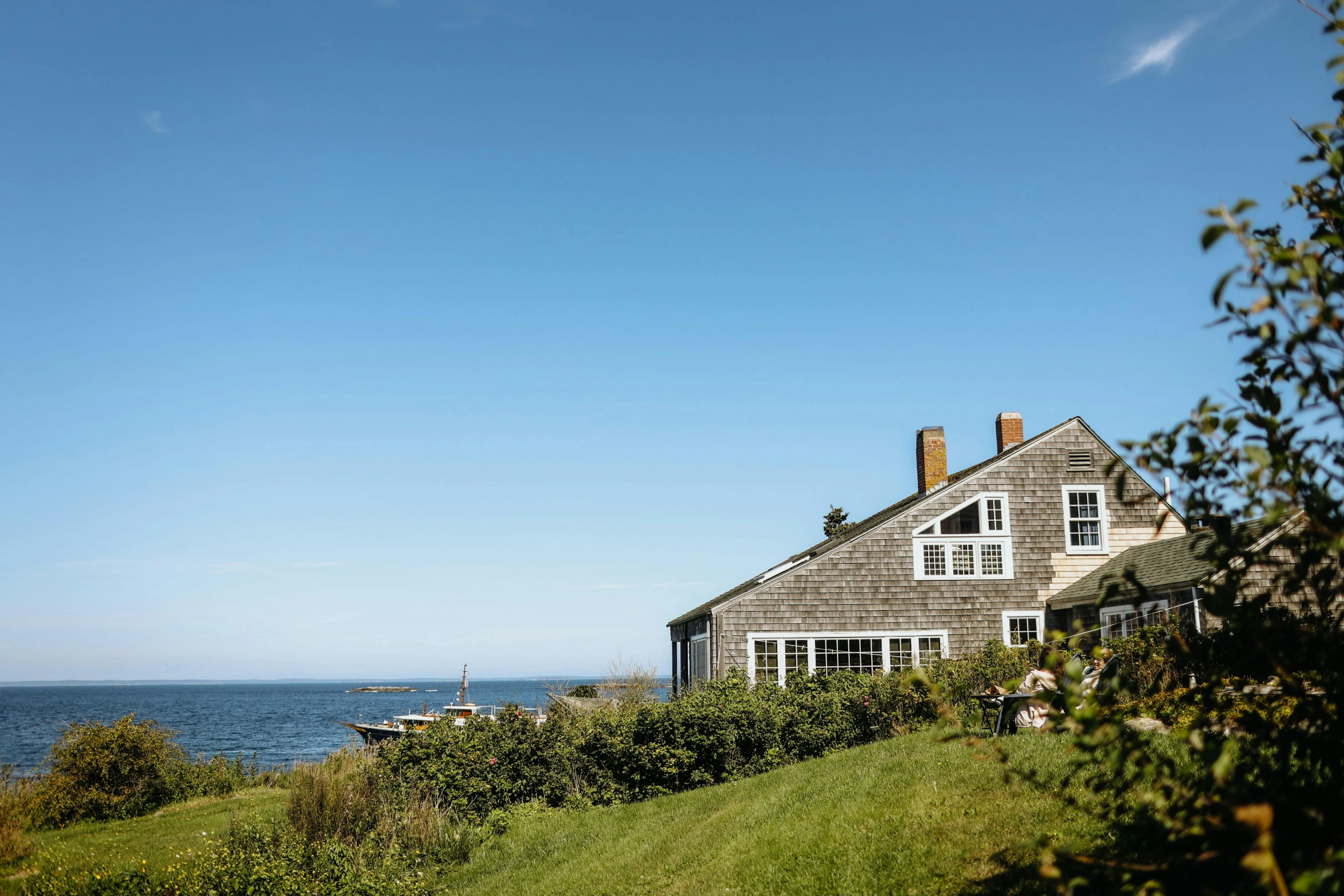 a house next to a body of water on top of a green hillside