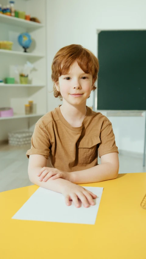 boy in brown shirt sitting at yellow desk smiling