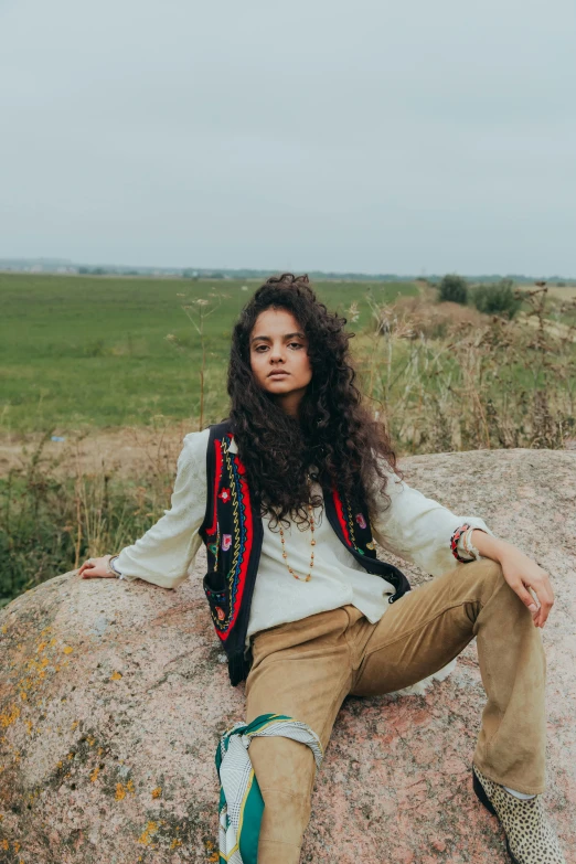 a woman sitting on top of a rock on a field