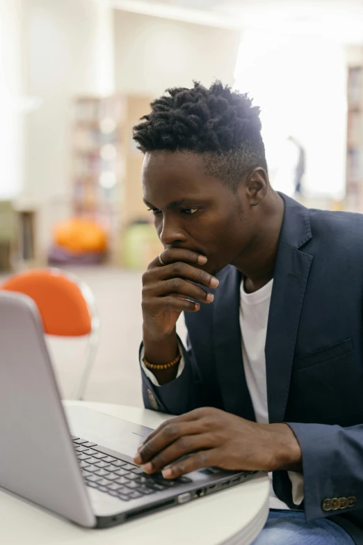 a person wearing a blue suit and tie sitting in front of a laptop