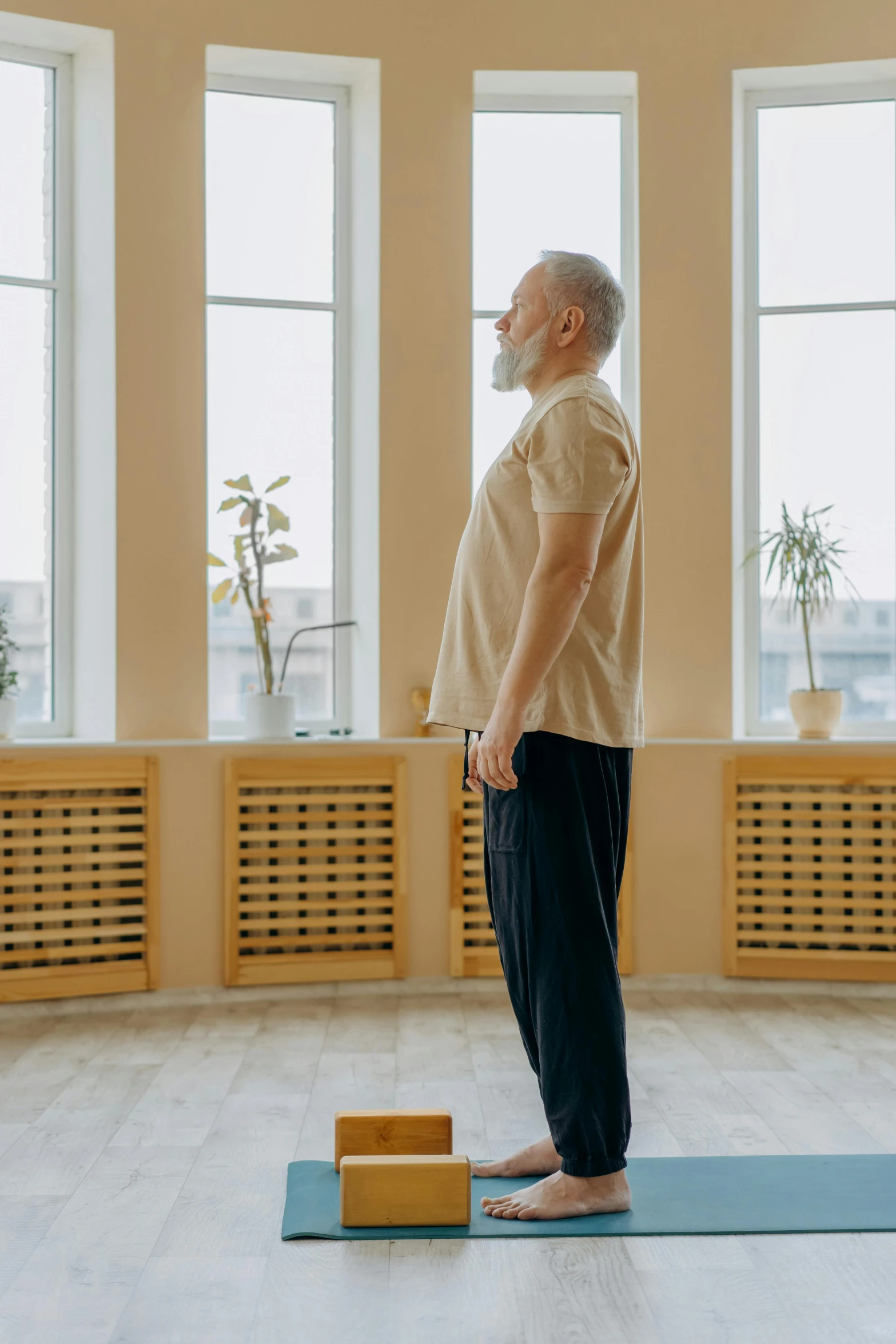 an old man with a beard stands on the mat and holds his back as he leans toward a brick