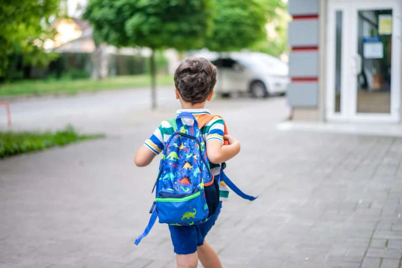 a boy wearing a blue backpack walks in front of a store