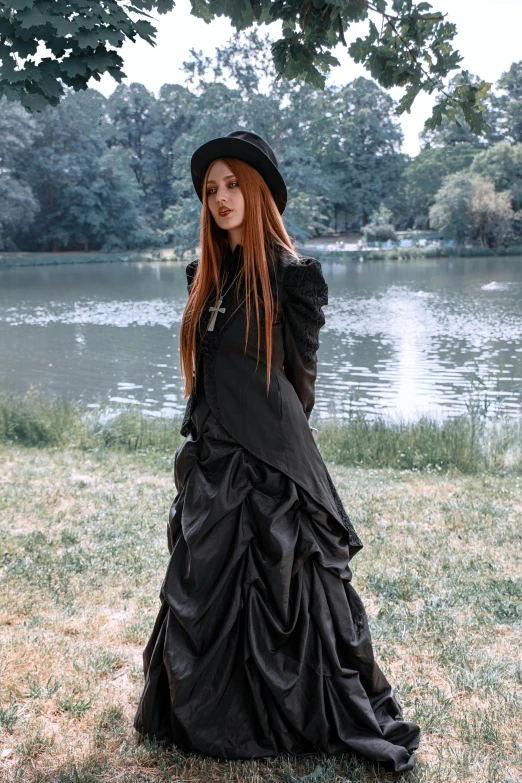 a lady in long dress by the water with hat