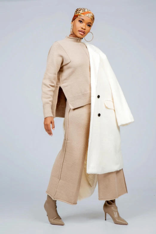 a woman standing in a white coat, beige pants and boots