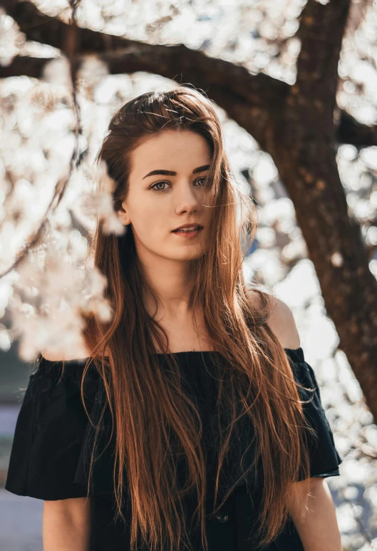 a  with long hair, wearing black dress and posing under a tree