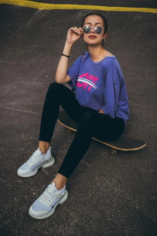 girl with sunglasses sitting on skateboard and looking up