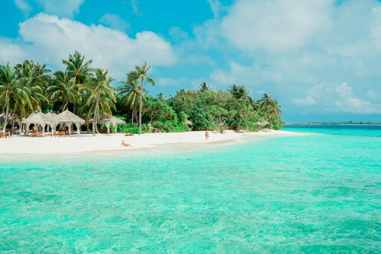 a beach with thatched huts, blue water, and some palm trees