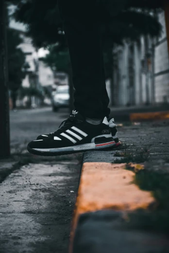 a person's foot standing on the street while wearing adidas