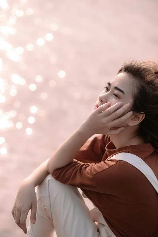 a beautiful young woman sitting next to a body of water