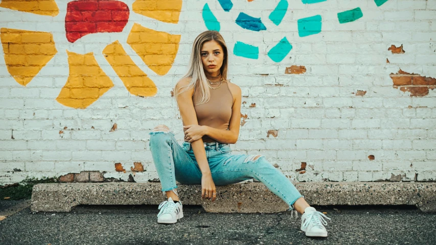 a young woman sitting on the street near a graffiti wall