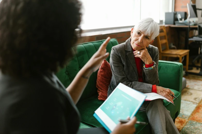 an older woman holding a note in one hand and talking to a younger woman