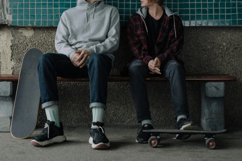 two people sitting on a bench next to a skateboard