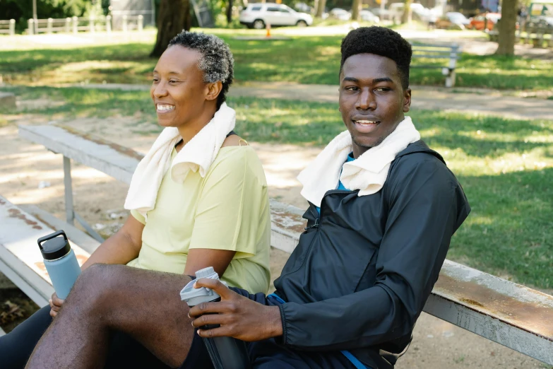 two people sitting on a wooden bench near some grass