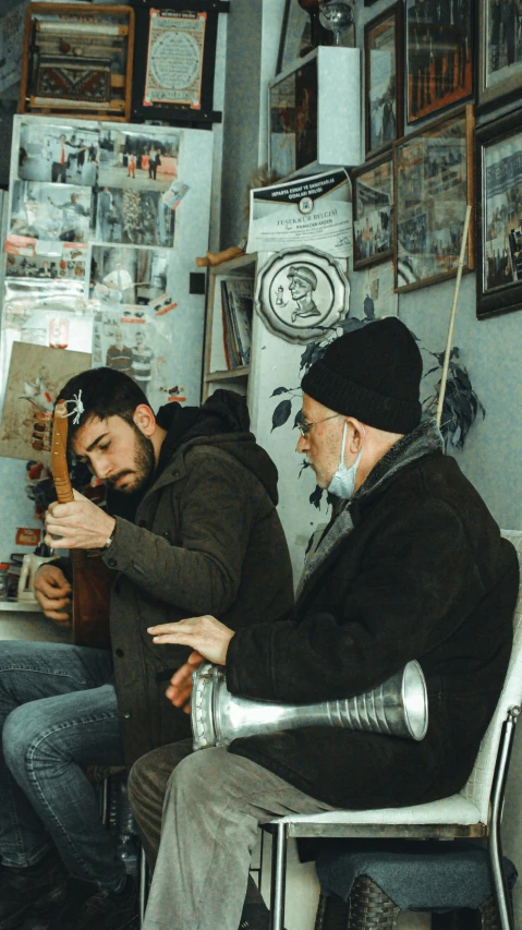 two men sit next to each other while one plays an instrument