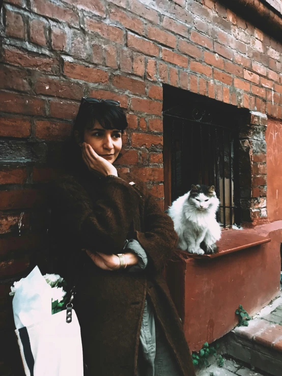 a woman leaning against a brick wall with her dog on a leash