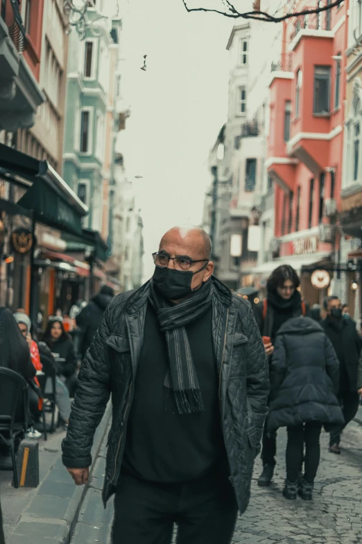 a man in a black hoodie and a black mask walks down an alley