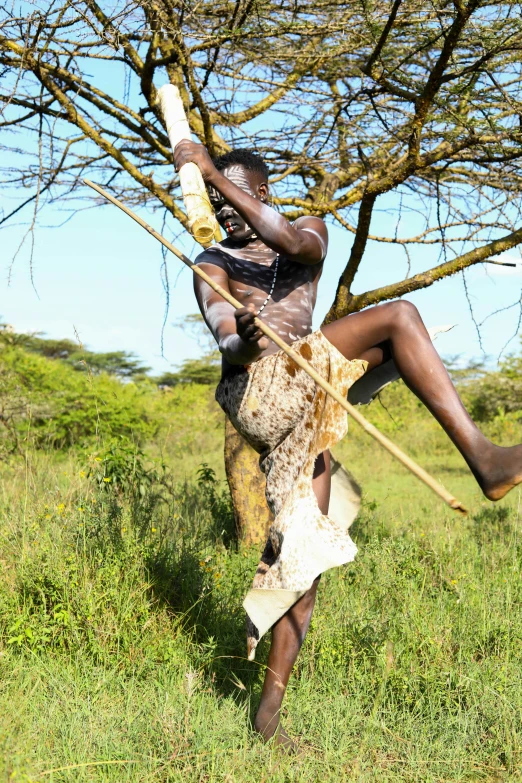 a man in a tribal dress is hanging from a tree with his hands and a wooden pole