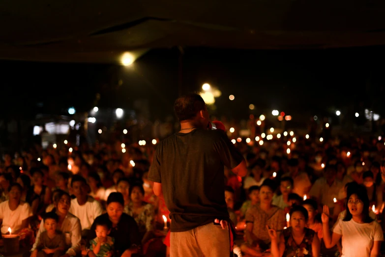 a man standing in front of a large crowd holding candles