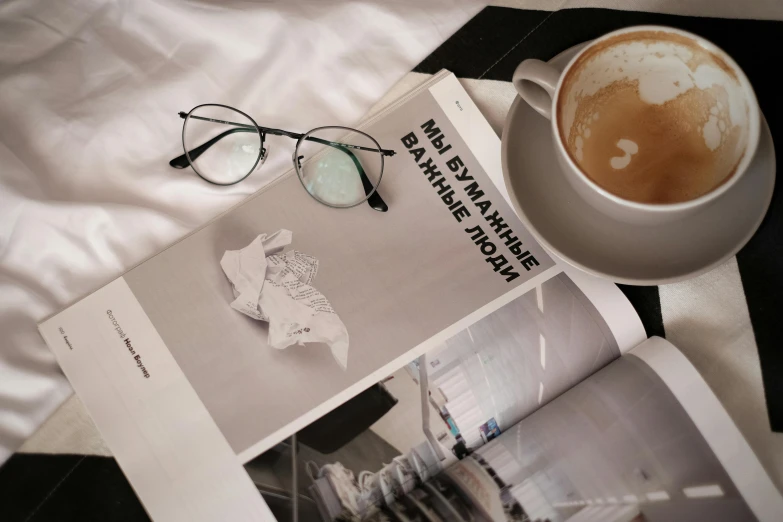 a pair of glasses, eye glasses and magazine are laying on a bed