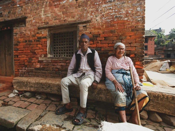 an older couple sitting on a bench in front of a building