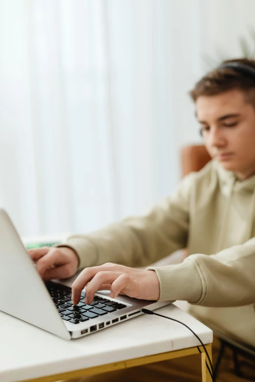 a young man uses a laptop while sitting at a desk