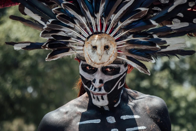 a man with white paint on his face and body has feathers in the background