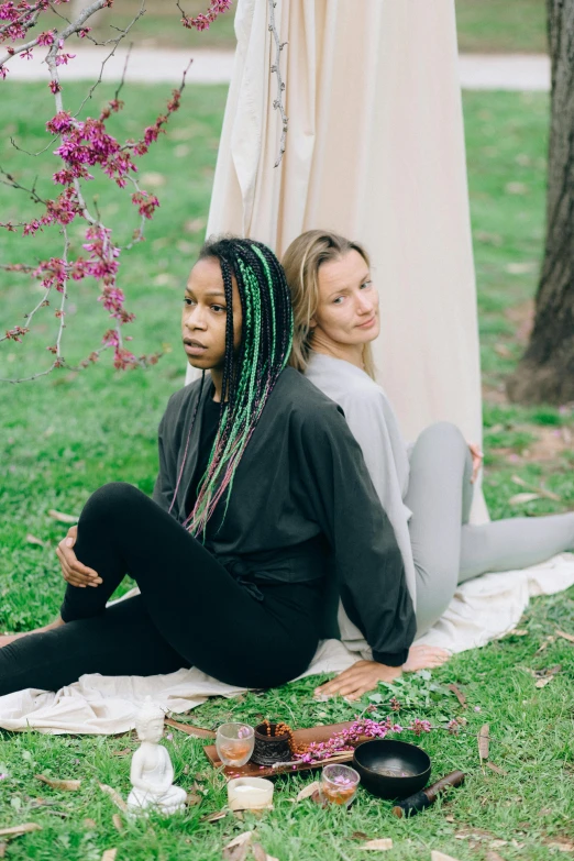 two beautiful young women sitting on the ground under a tree