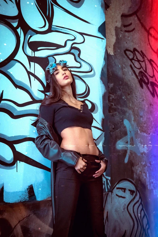 a young woman in black leather clothes and sunglasses posing next to graffiti covered wall