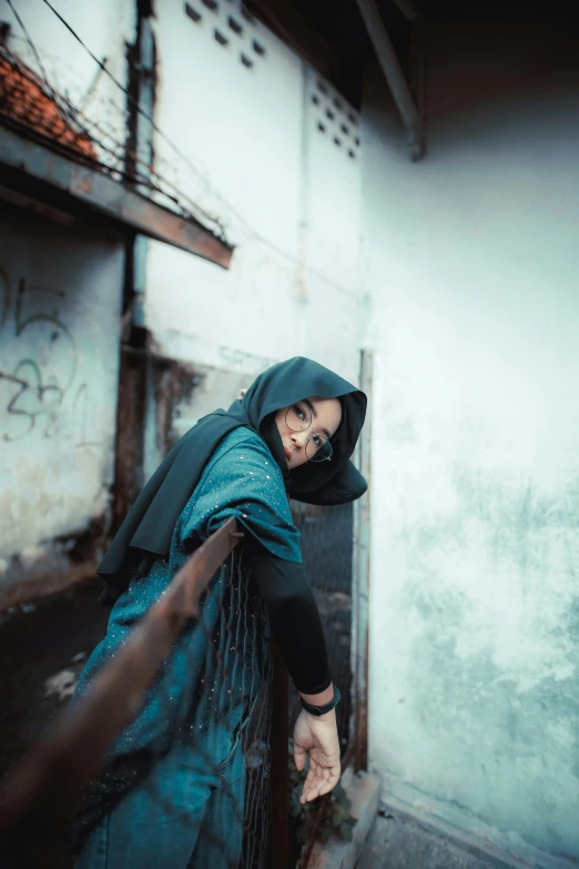 a woman in green headscarf leaning up against a fence