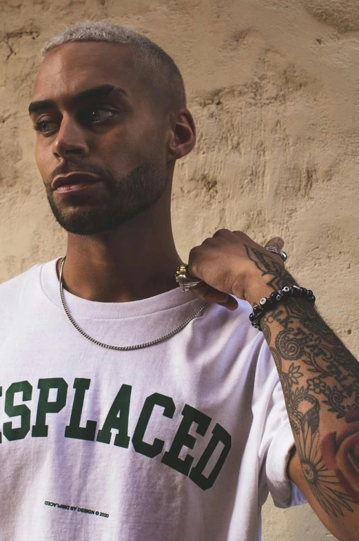 a man standing in front of a wall wearing a white t - shirt with an unpllaced message