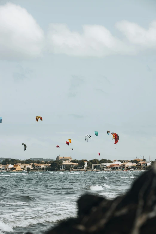 kites in the sky over the water in front of some houses