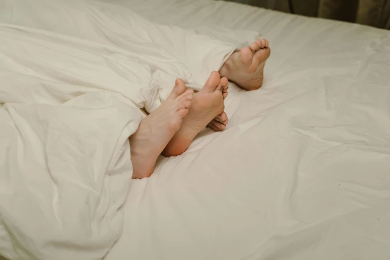 two legs sticking out of an unmade bed with white sheets