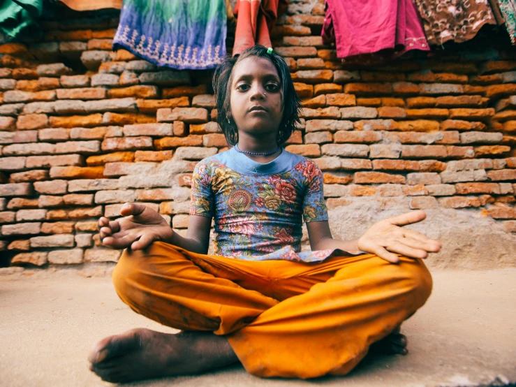 a girl sitting in a bright orange colored outfit meditating in a room